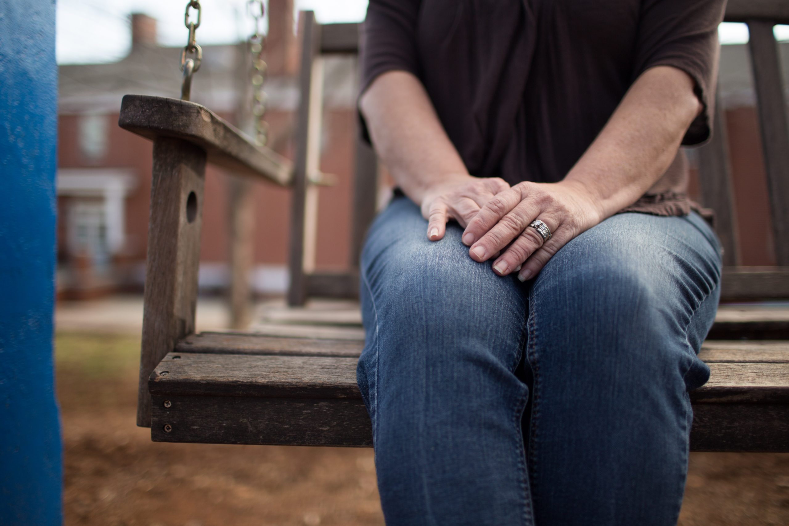 Person sitting on wooden swing hands clasped on lap silver ring