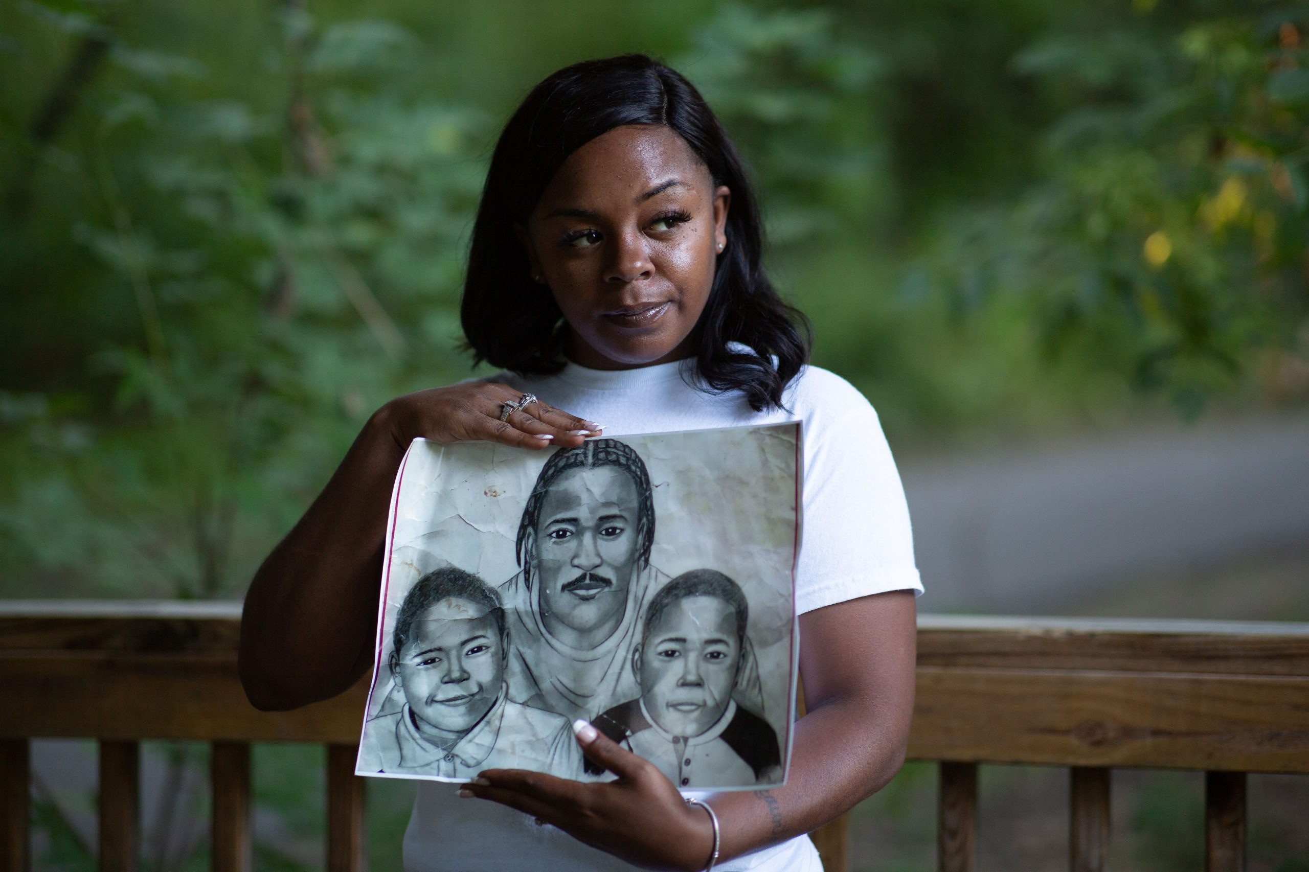 Woman posing in park with the charcoal-drawn portraits of her children and their currently-incarcerated father