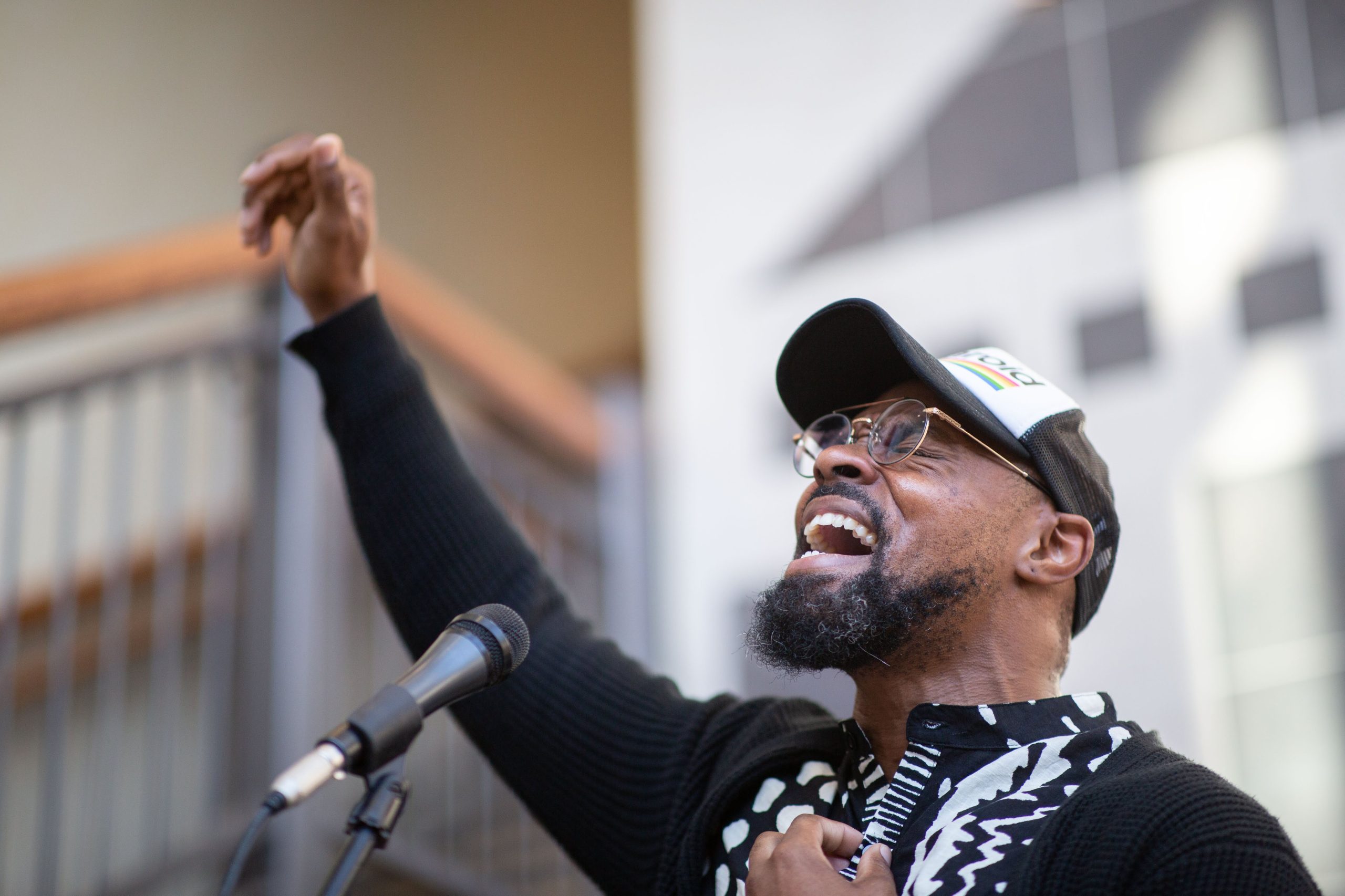 Black man with beard and white hat, singing into mic and holding right hand into hair, overcome with emotion