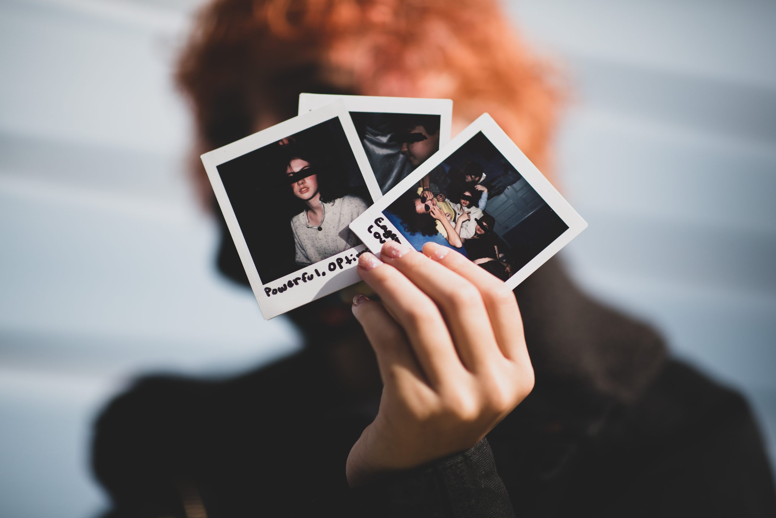 young person with dyed orange hair holding three polaroids in front of their face