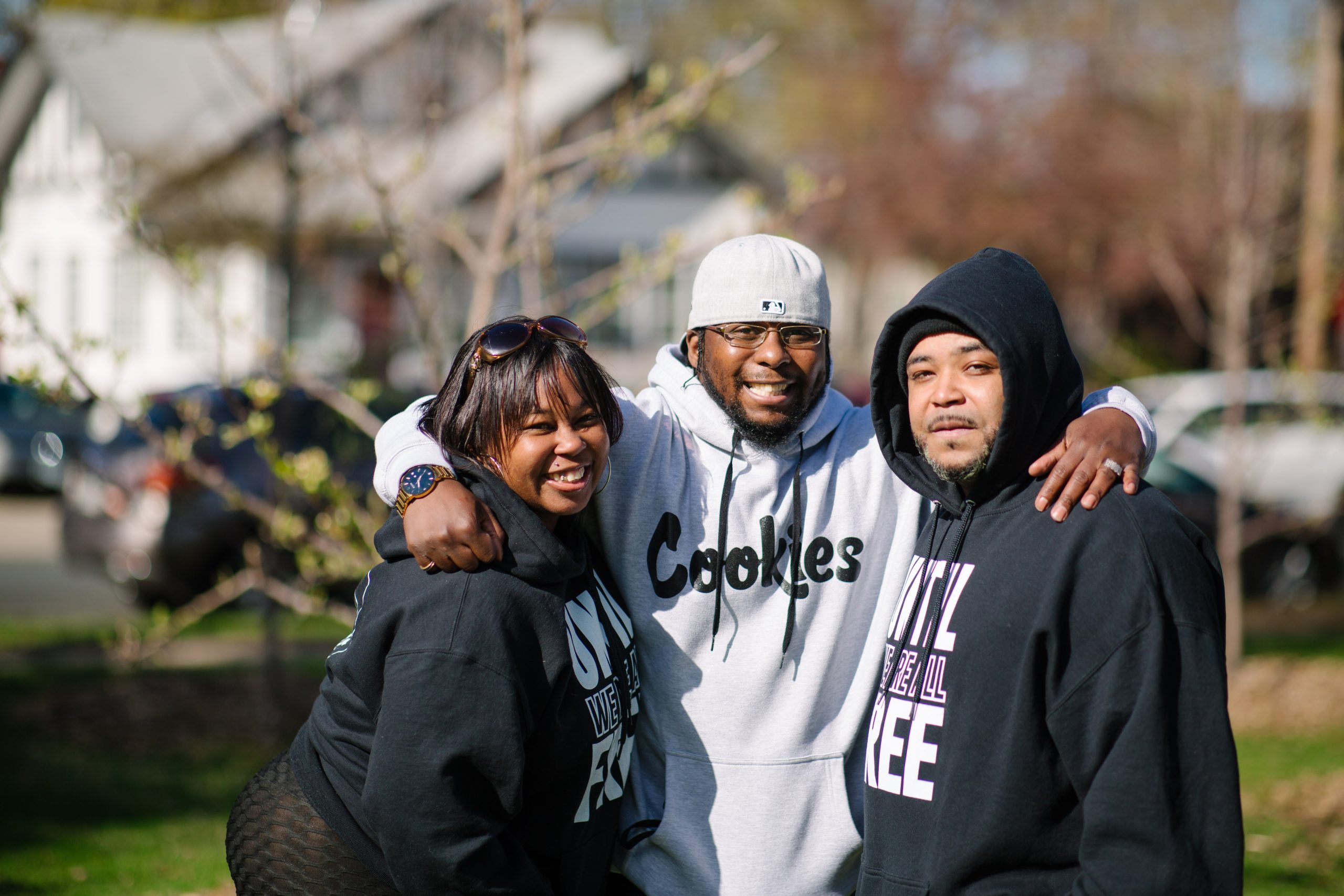 Three people in Until We Are All Free Hoodies smiling and looking directly at camera. It's a sunny, chilly day.