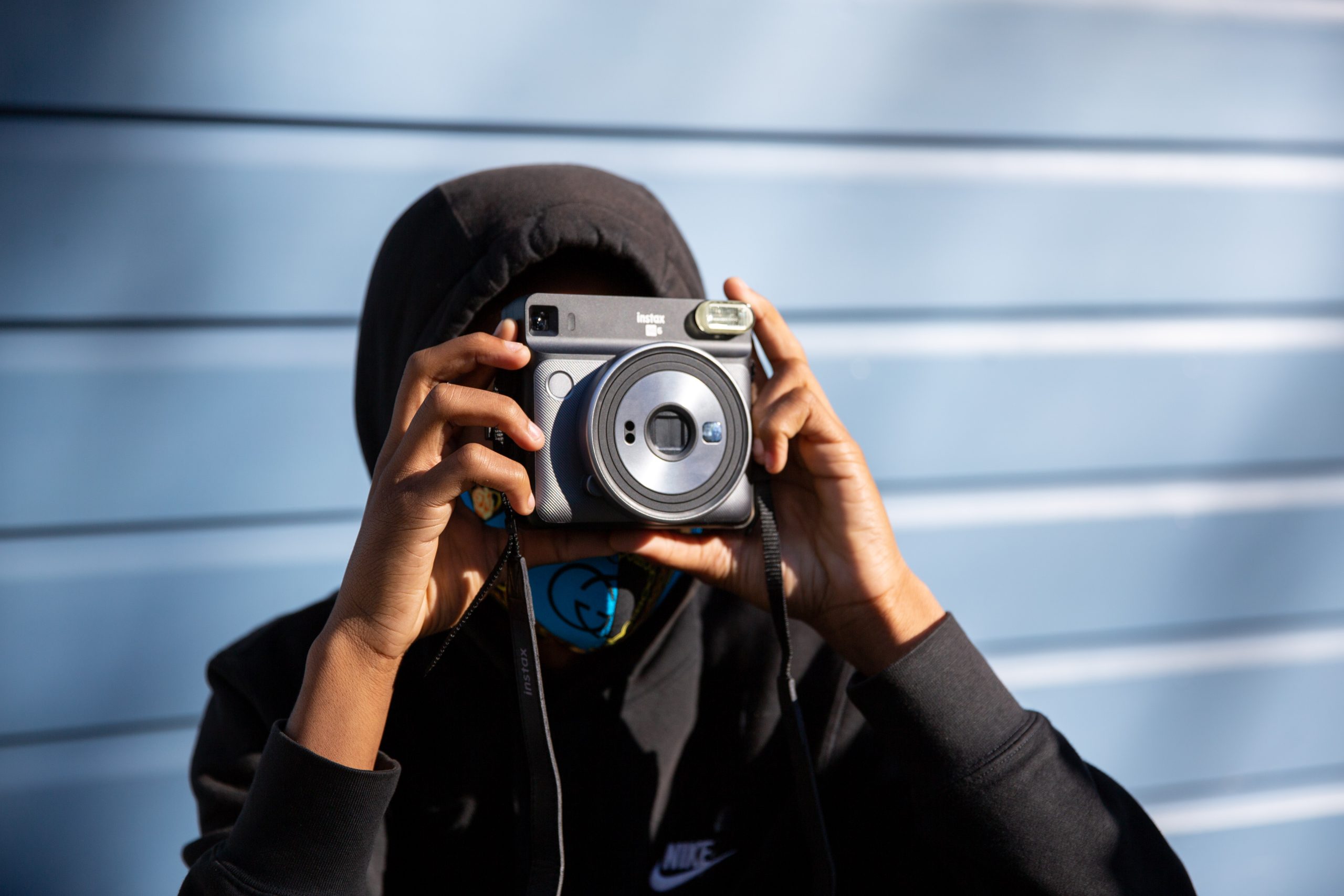 young Black man holding blue polaroid camera, face obscured