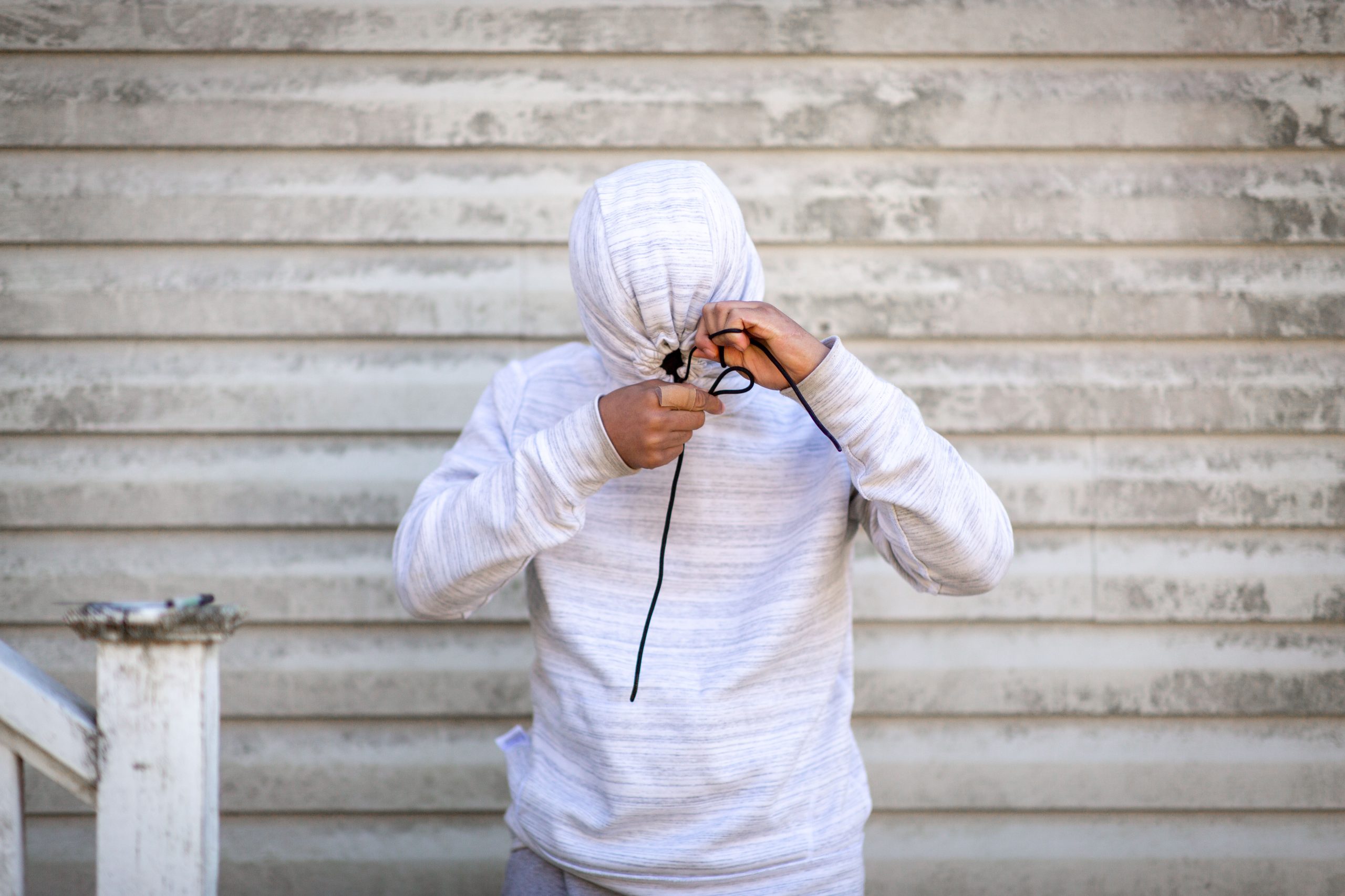 young man pulling strings on white hoodie tight, obstructing view of face