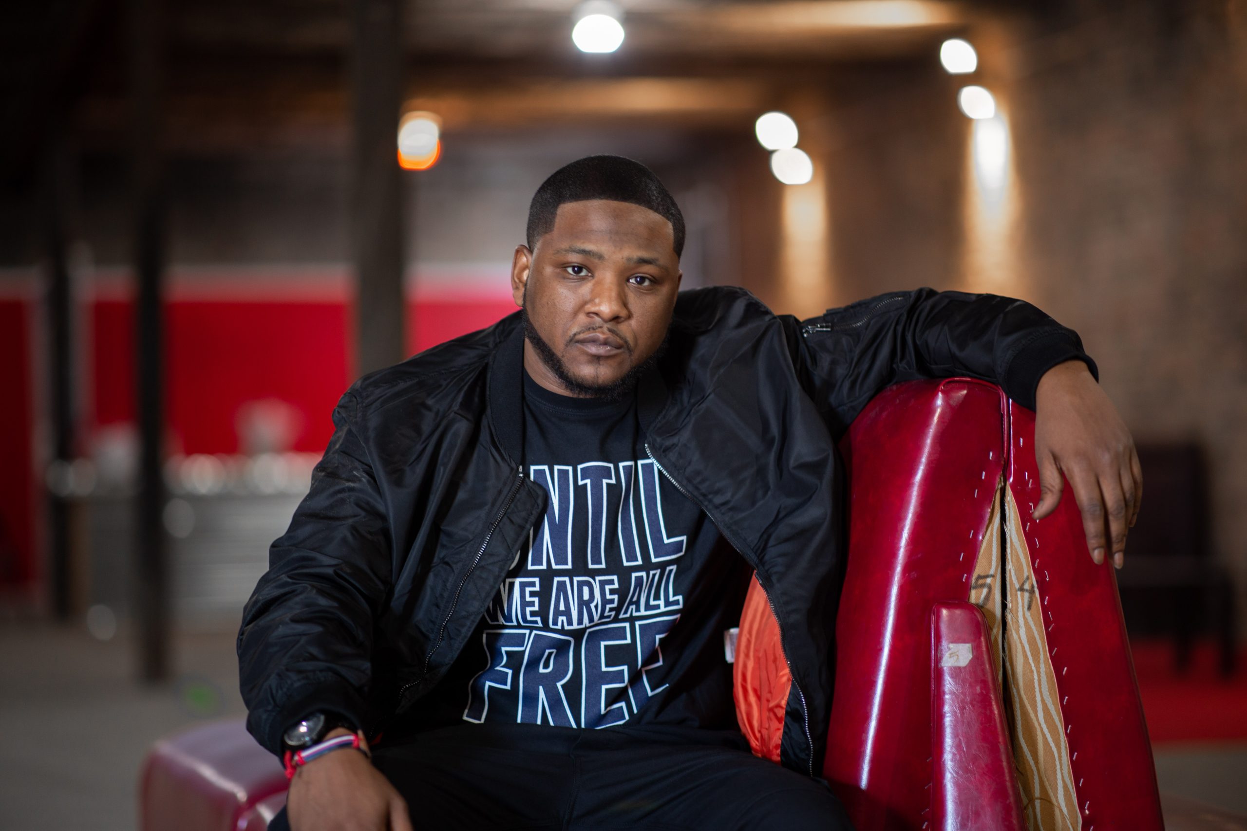 Kevin Reese seated on a red bench in a warehouse, looking directly at camera