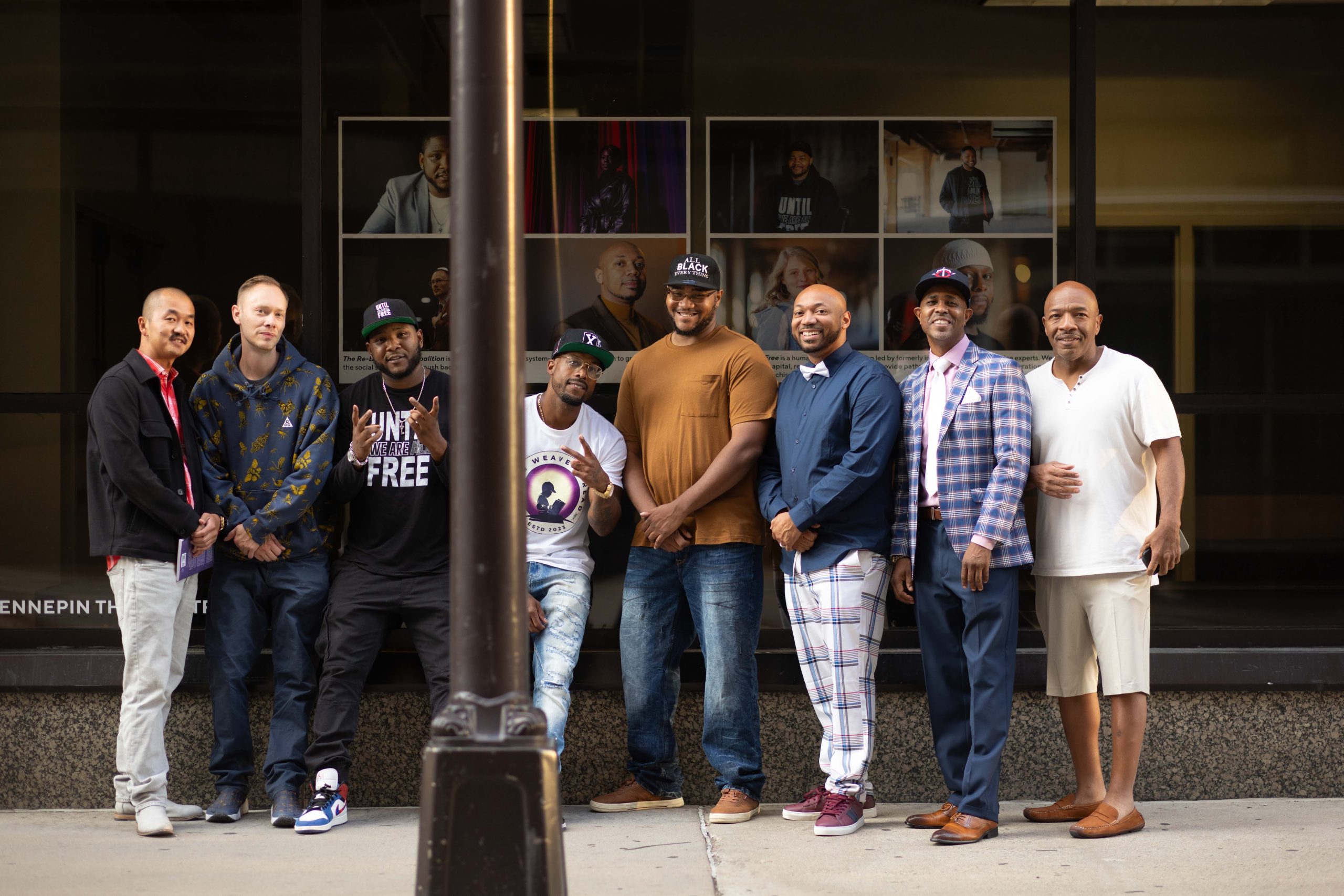 Eight people in front of WAAC photos at the Hennepin Theatre Trust's sidewalk art gallery