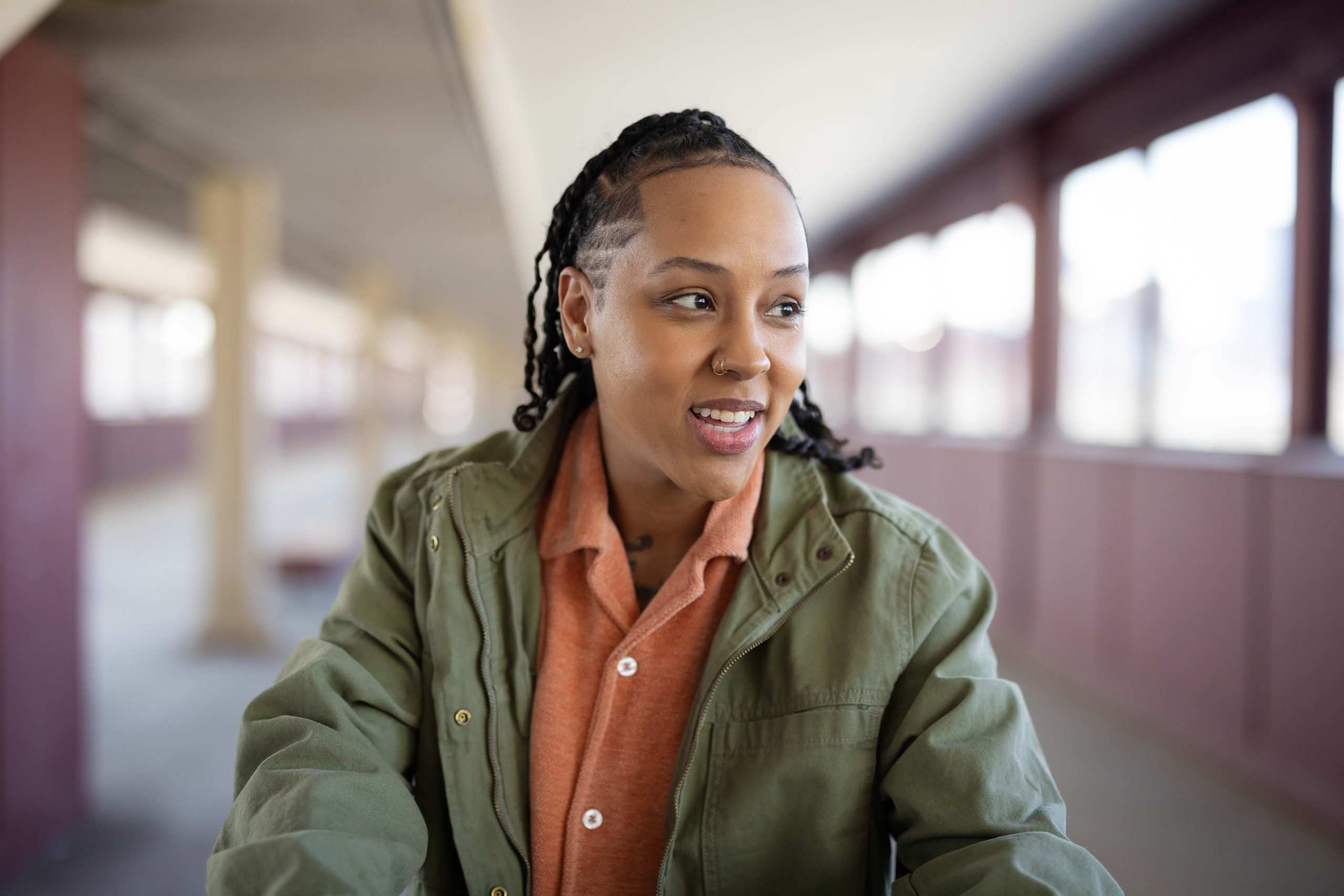 Artist Lux standing in the pedestrian bridge on Washington Ave in Minneapolis, wearing a green jacket and looking to her left