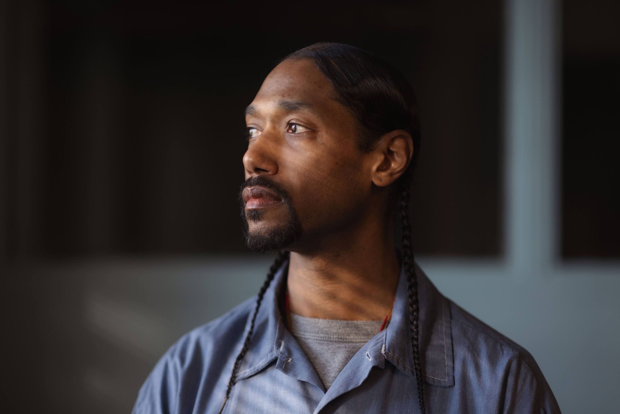 Small child in shorts, t-shirt, and rain boots, standing in a playing field next to a soccer net, holding a large yellow rubber ball in front of her face
