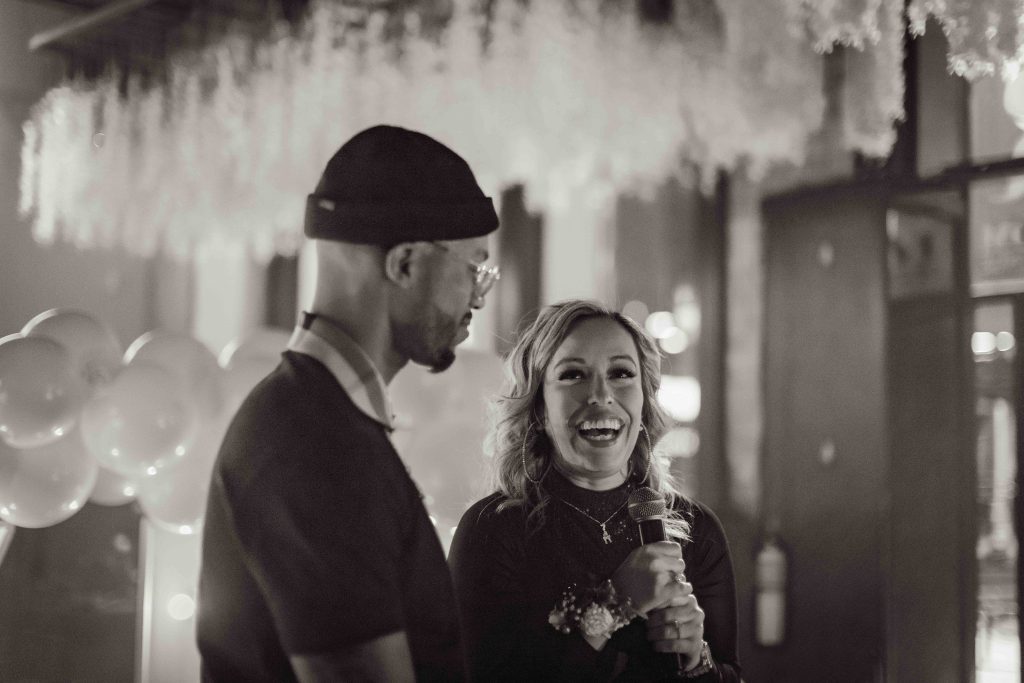 Leslie and Antonio smiling and speaking into a microphone, in black and white