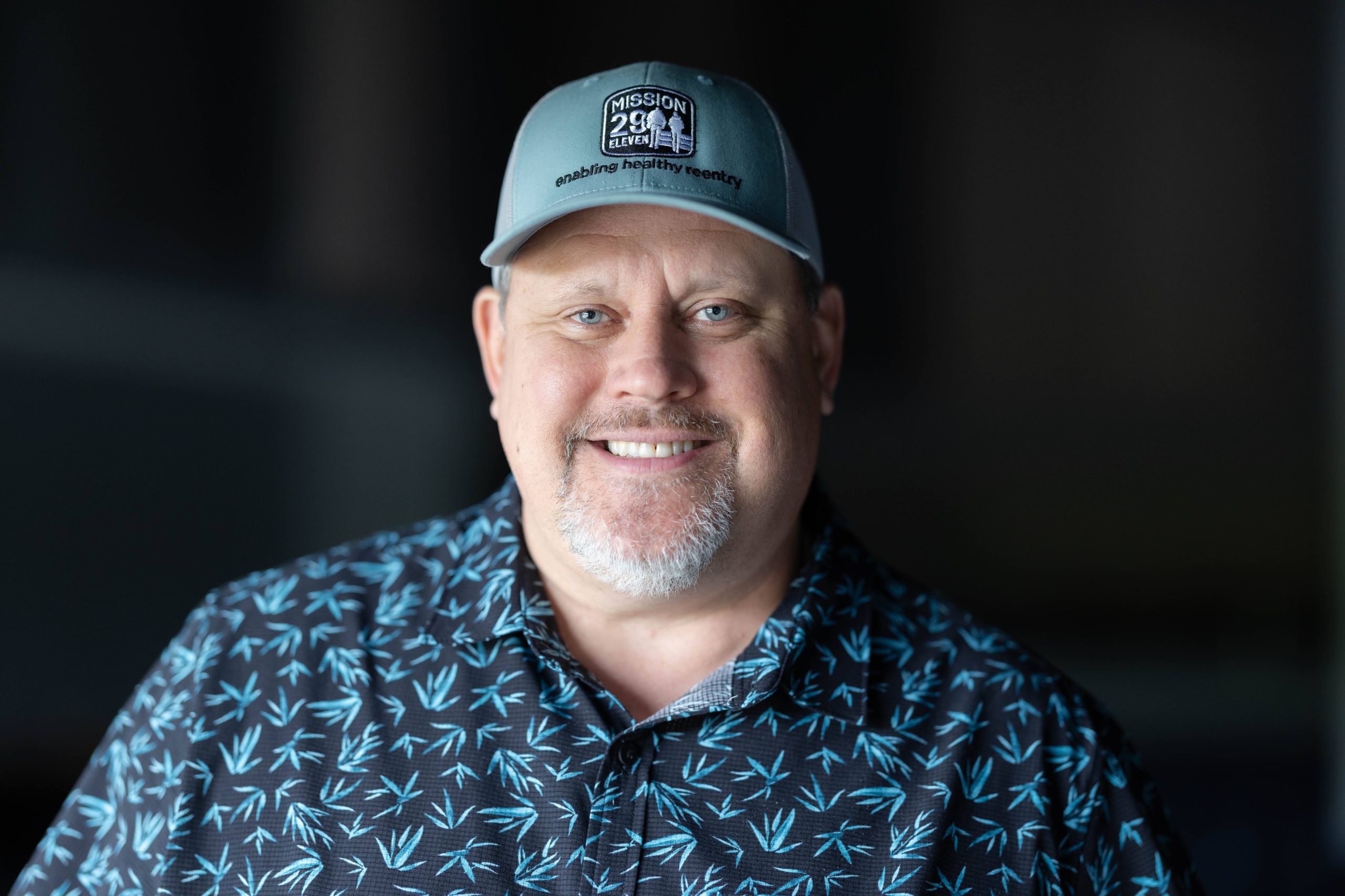 Man in teal shirt and hat, reading Mission 29:11 Reentry, smiling at the camera